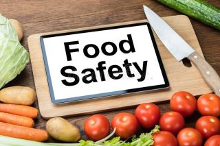 Image of a cutting board and produce with the words "food safety" written on it.